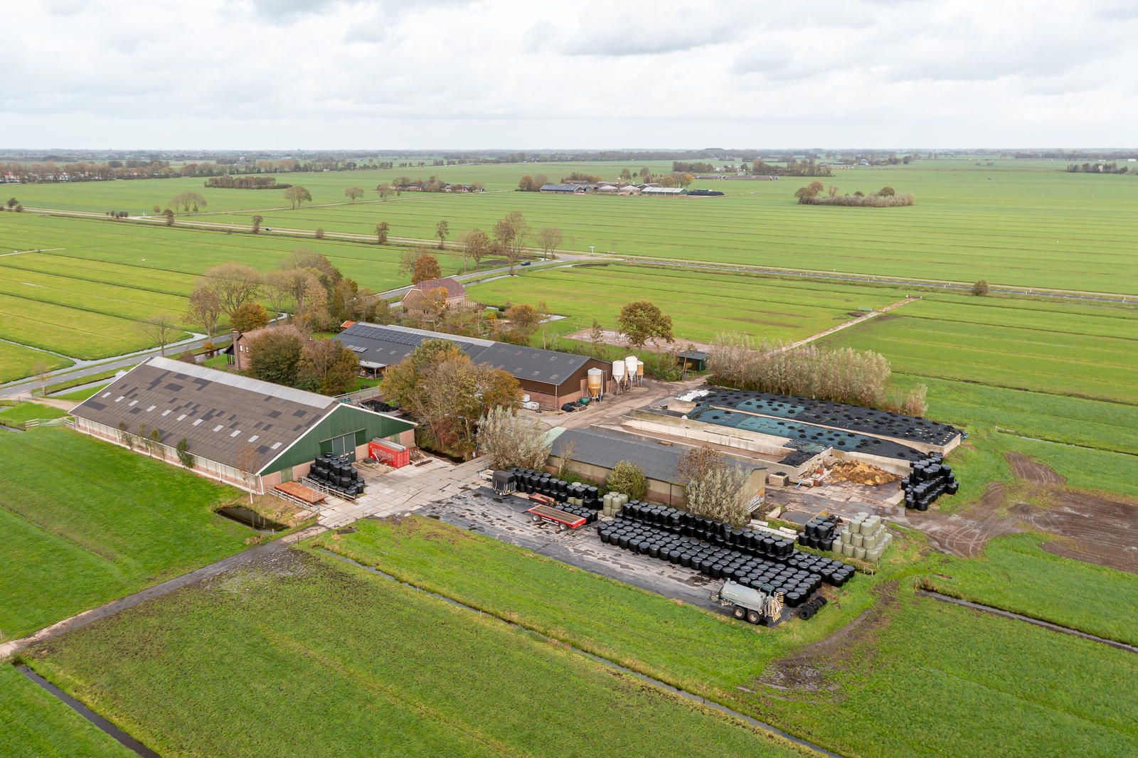 Luchtfoto van een agrarisch bedrijf met stallen, sleufsilo's en weilanden