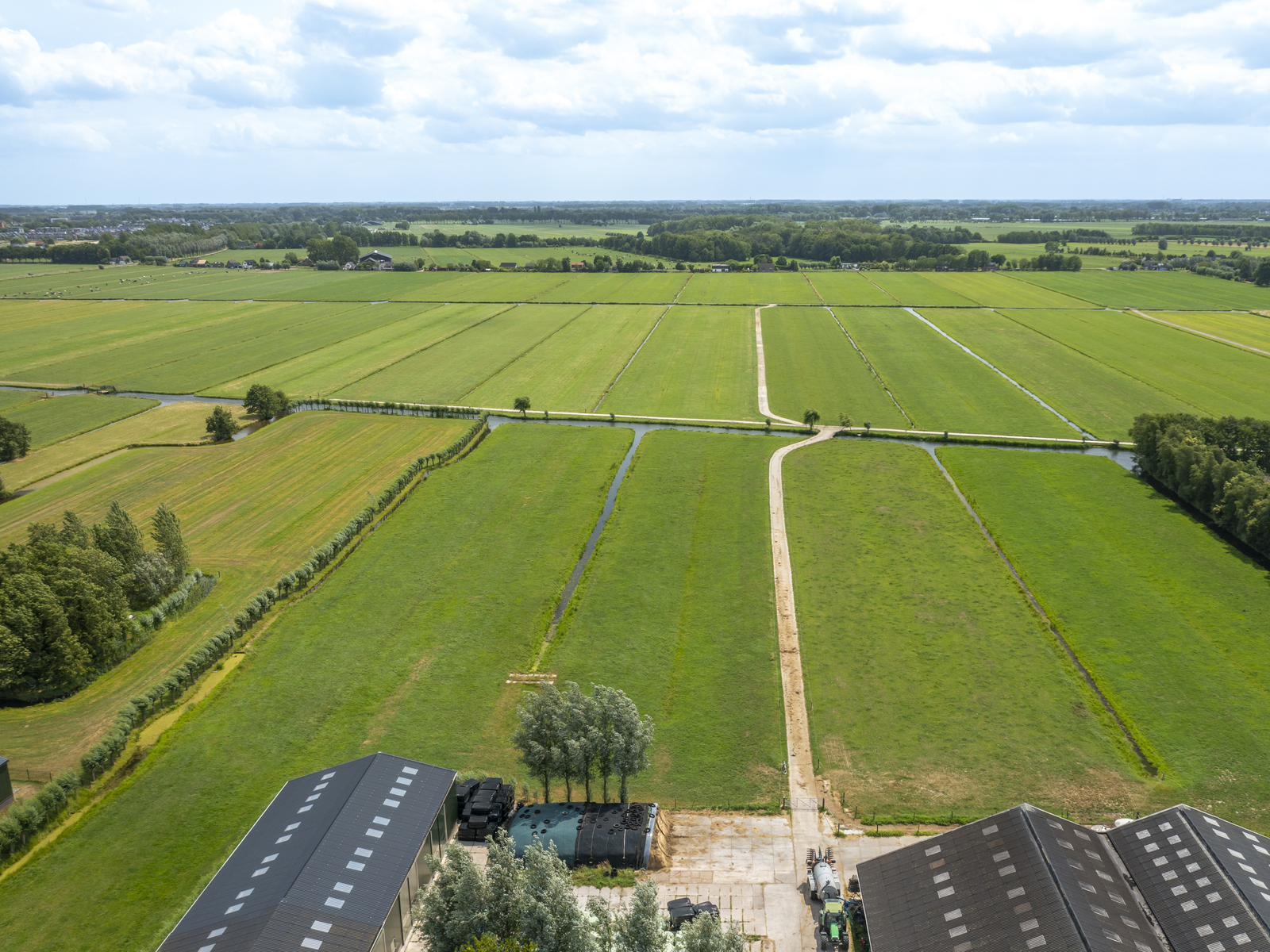 Luchtfoto van landbouwgrond met kavels, sloten en een ontsluitingspad achter agrarische bedrijfsgebouwen