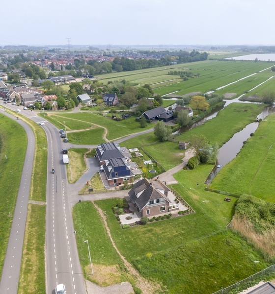 Luchtfoto van een dijk met woningen en weilanden met sloten in het rivierengebied